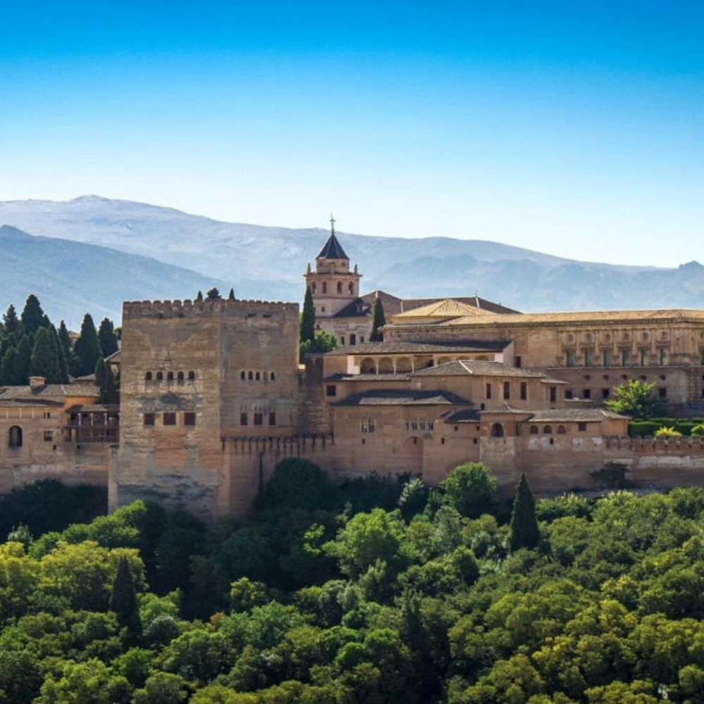 The majestic Alhambra fortress in Granada, Spain, surrounded by lush greenery and mountains under a clear blue sky.