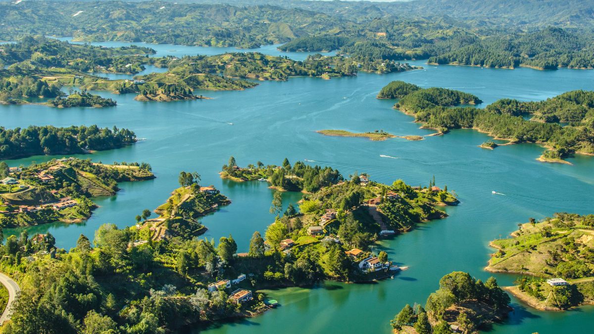 Aerial view of a scenic landscape featuring lush green hills and numerous small islands amidst a tranquil blue lake. The area is dotted with houses and trees, reflecting a serene natural environment.