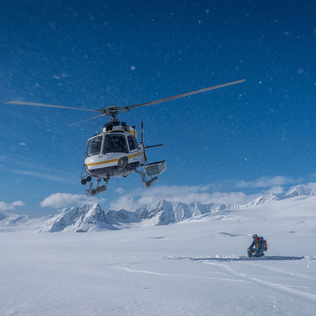 White helicopter landing on icy Greenland terrain with crew on ice – Pelorus Yachting 2026 Arctic luxury expedition.