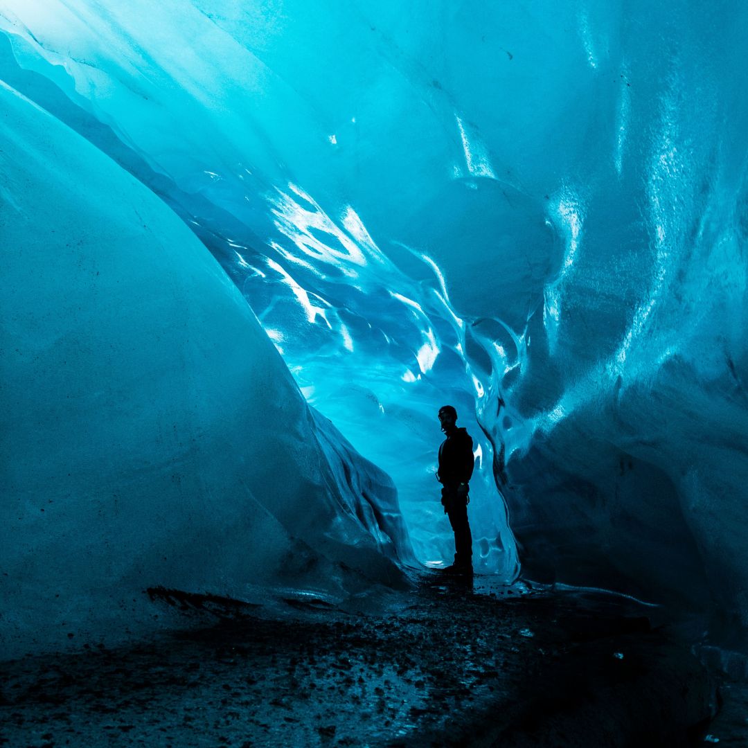 Silhouette of a person standing inside a glowing blue glacial ice cave.
