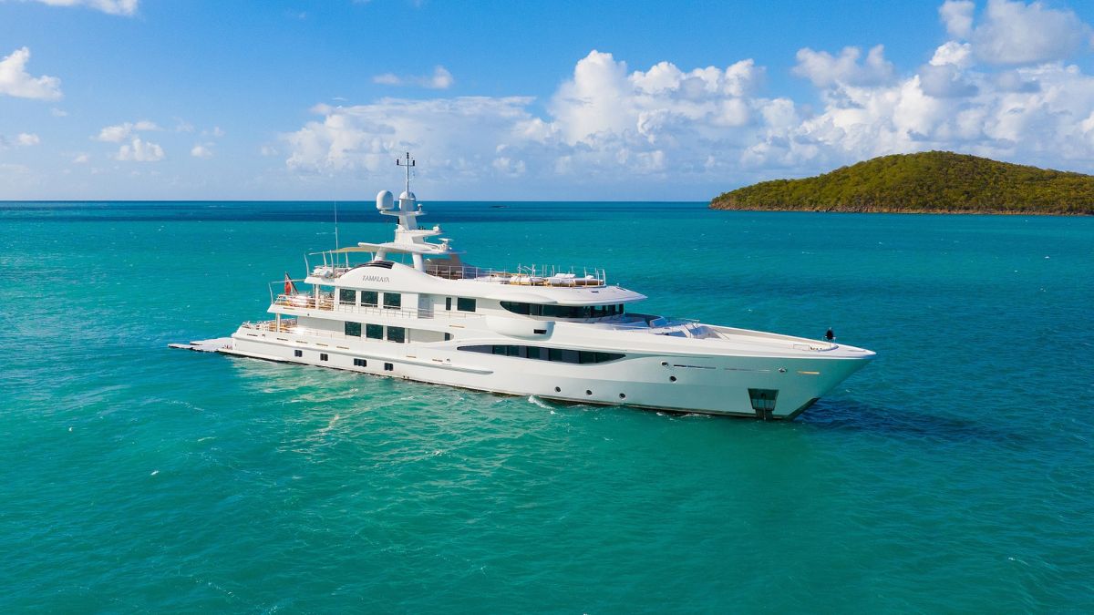 Sleek white yacht sailing through vibrant turquoise water under a blue sky with fluffy white clouds.