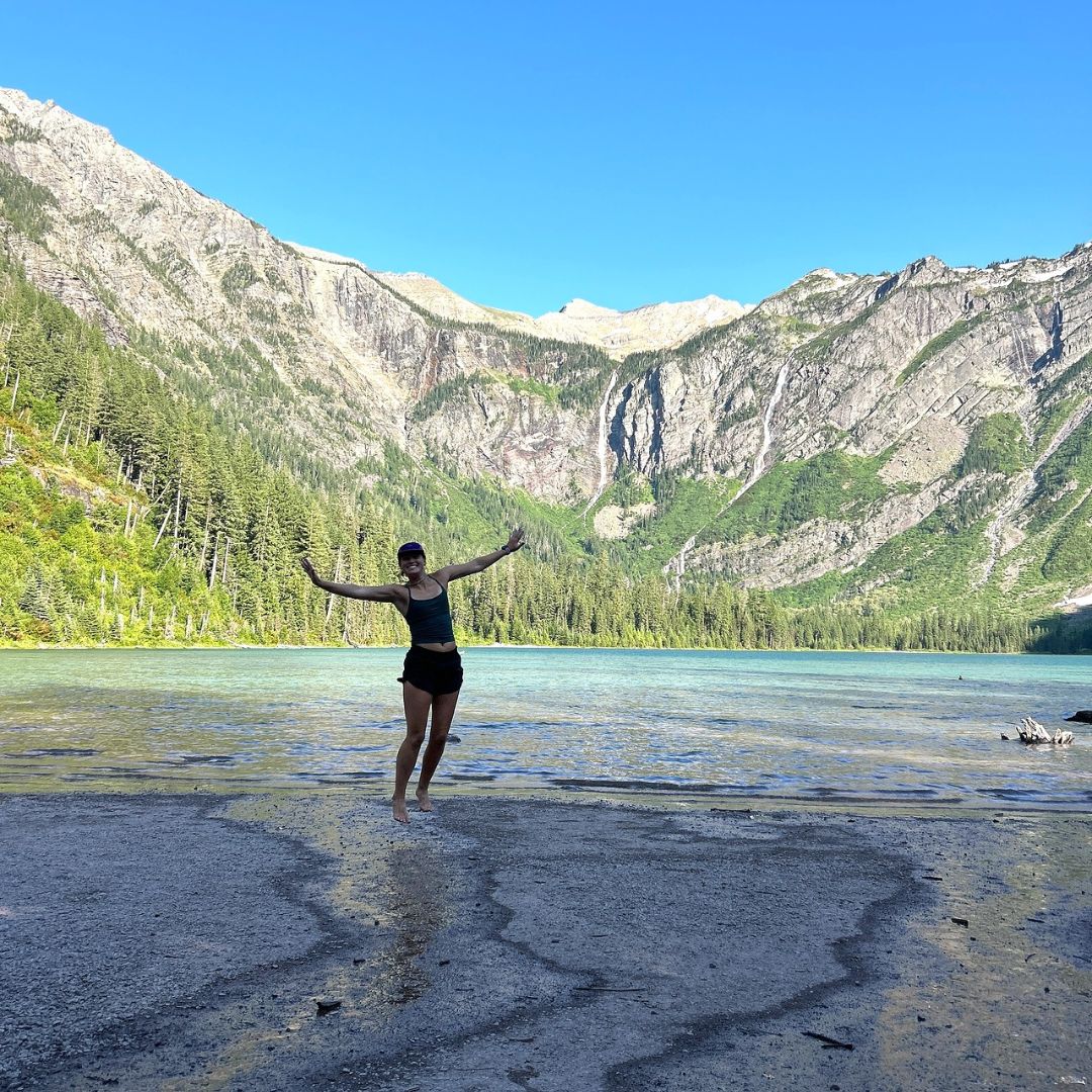 Molly Bradach jumping by blue lake and mountain range