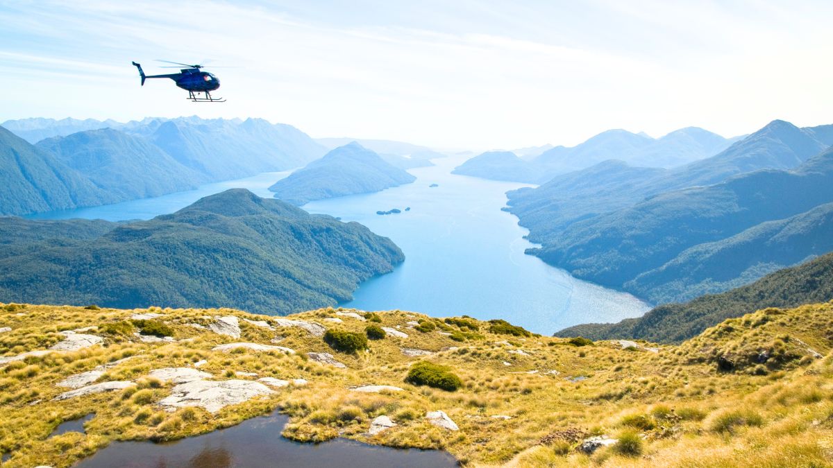 A helicopter flying over a scenic hillside in New Zealand, ready for a luxury travel concierge experience with breathtaking views of the mountains and valleys.