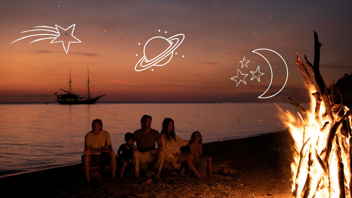 A family sits by a beach bonfire at sunset, with a silhouette of a sailing ship in the background. Illustrations of celestial elements like stars, a planet, and a crescent moon adorn the scene.