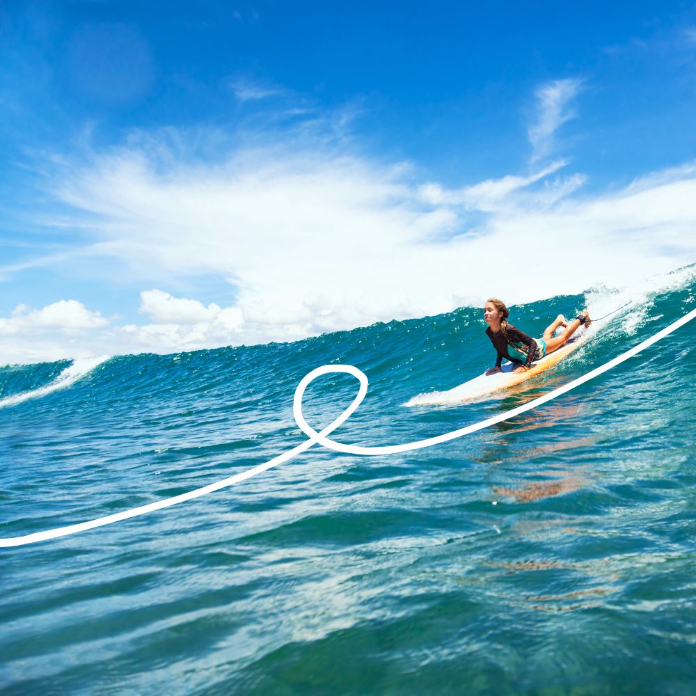 A surfer skillfully rides a wave under a bright blue sky with wispy clouds, creating a dynamic and lively scene.