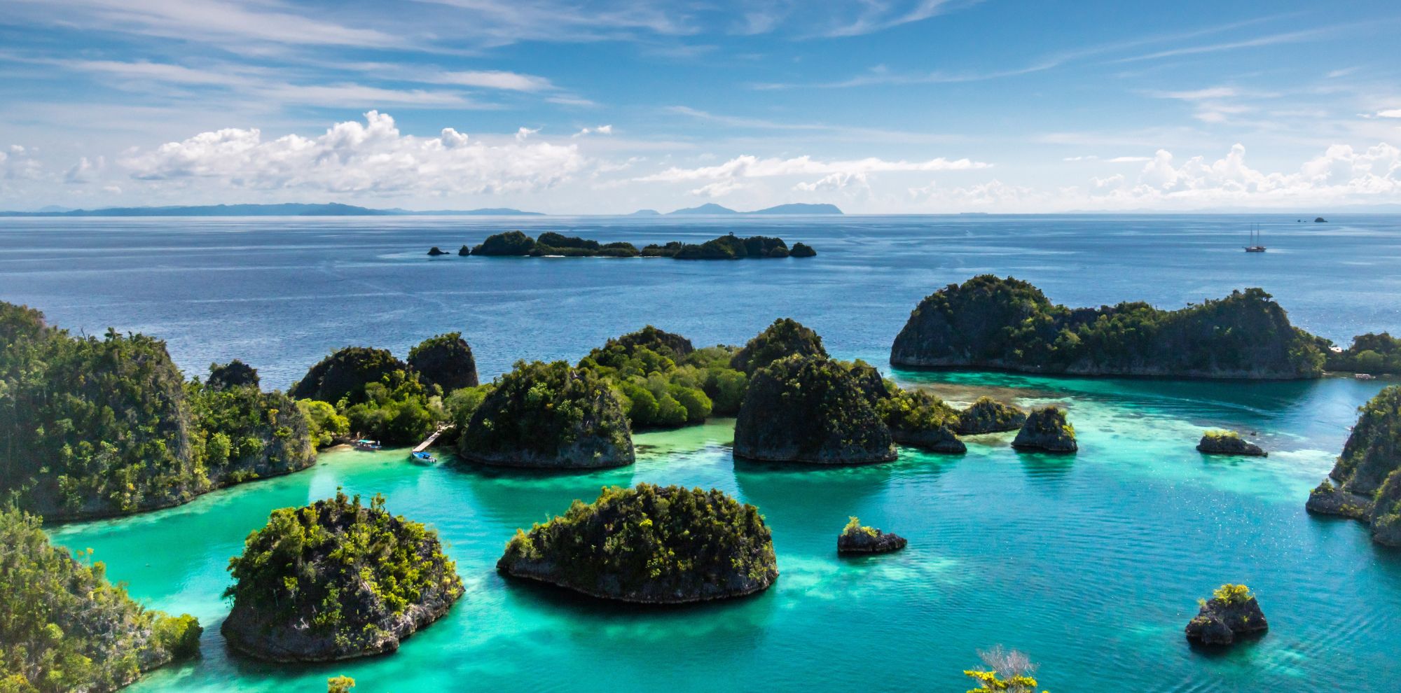 Lush, green limestone islands rise from a vibrant turquoise lagoon within a deep blue tropical ocean.