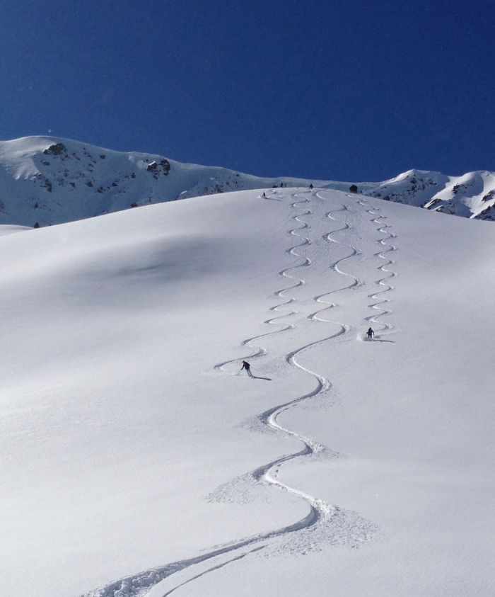 Ski tracks zigzag down a pristine snow-covered mountain under a clear blue sky.