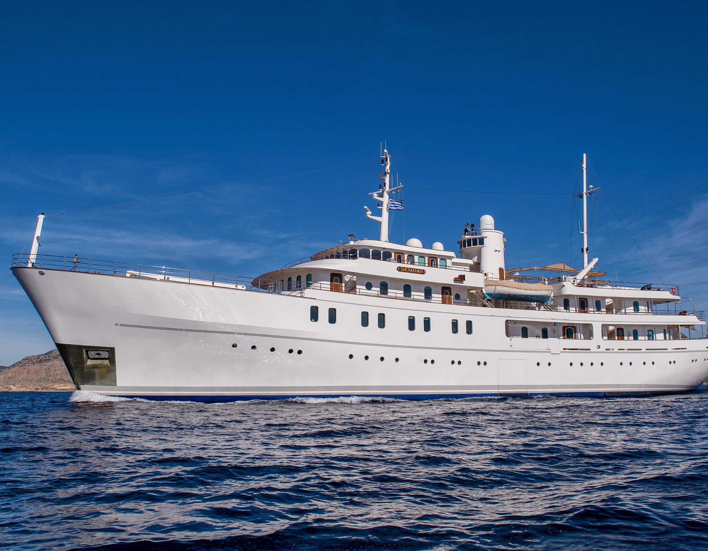 Large white classic motor yacht named SHERAKHAN cruising on deep blue water under a clear sky.