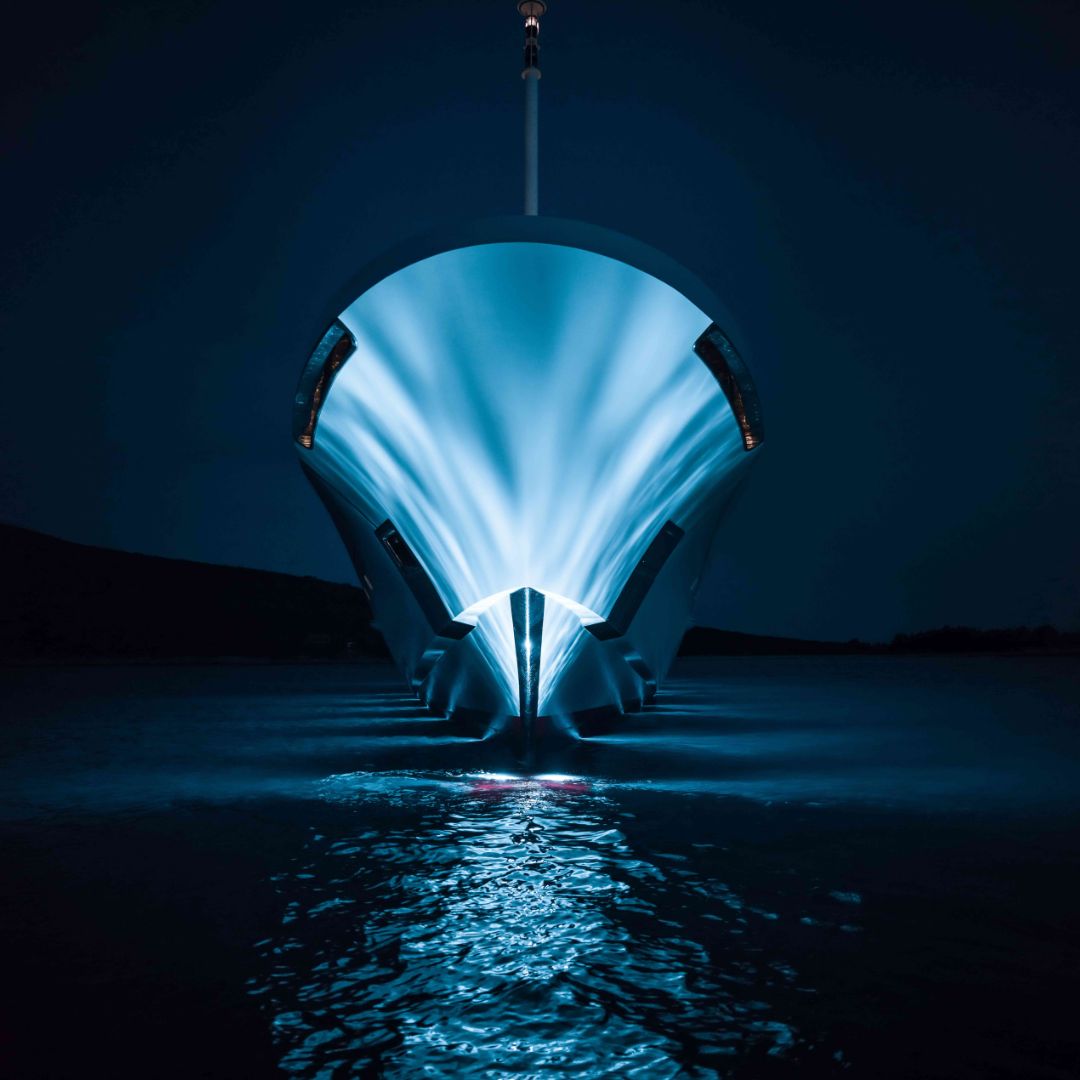 A sleek, modern boat with a luminous blue light emanating from the bow, cutting through dark water at night, creating a striking visual effect.