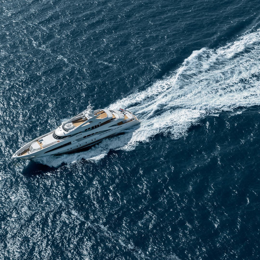 A sleek white yacht cruises through deep blue ocean waters, leaving a trail of frothy waves in its wake.