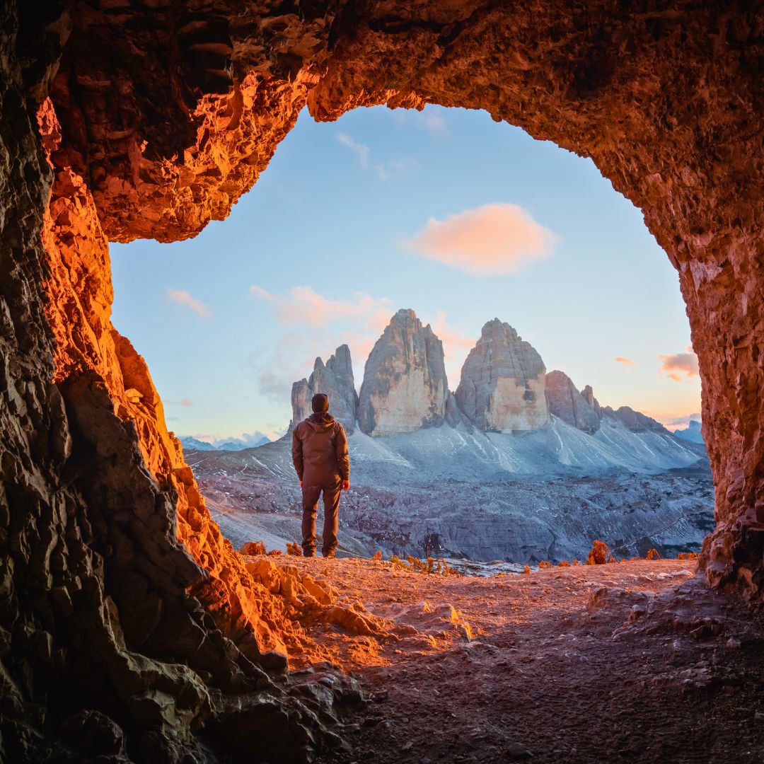 Man outside a mountain cave facing the Italian alps at sunrise
