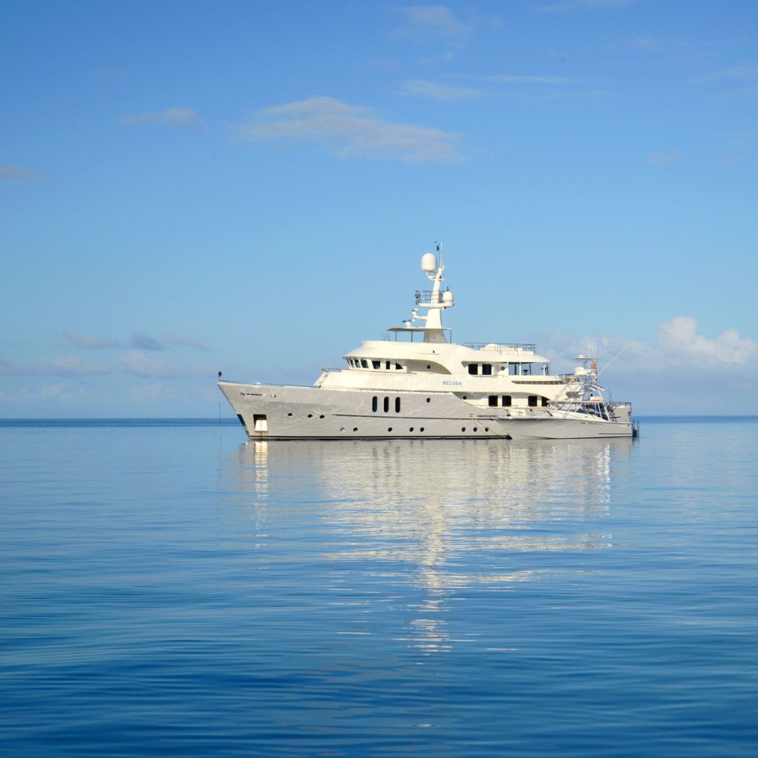 A large luxury yacht anchored in calm, blue waters under a clear sky. The yacht features multiple decks, large windows, and a sleek design.