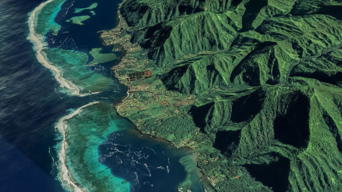 Aerial view of a lush, green mountainous landscape bordering a vibrant turquoise sea, with a small village nestled along the coastline.