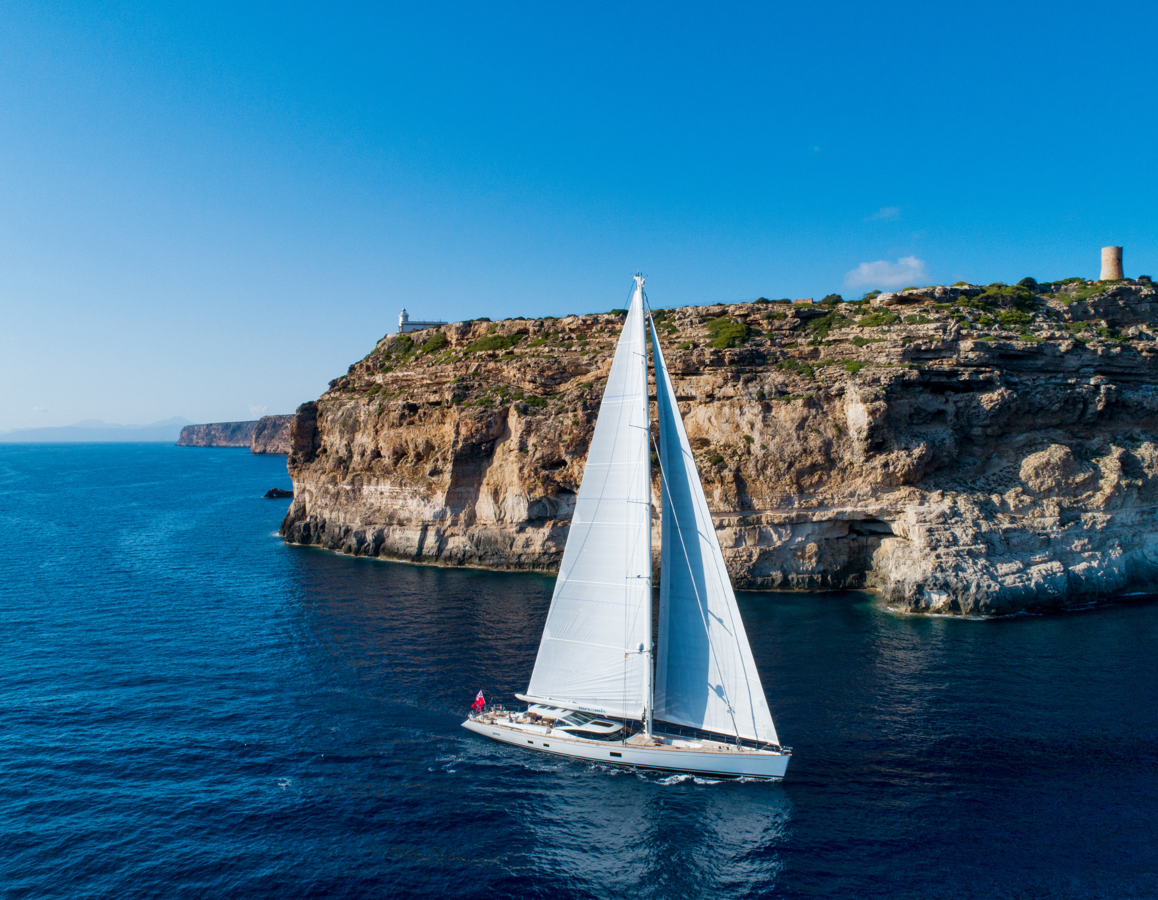 Luxury sailing yacht before dramatic rocky cliffs – Pelorus Yachting 2026 cinematic Odyssey voyage inspired by myth and film.