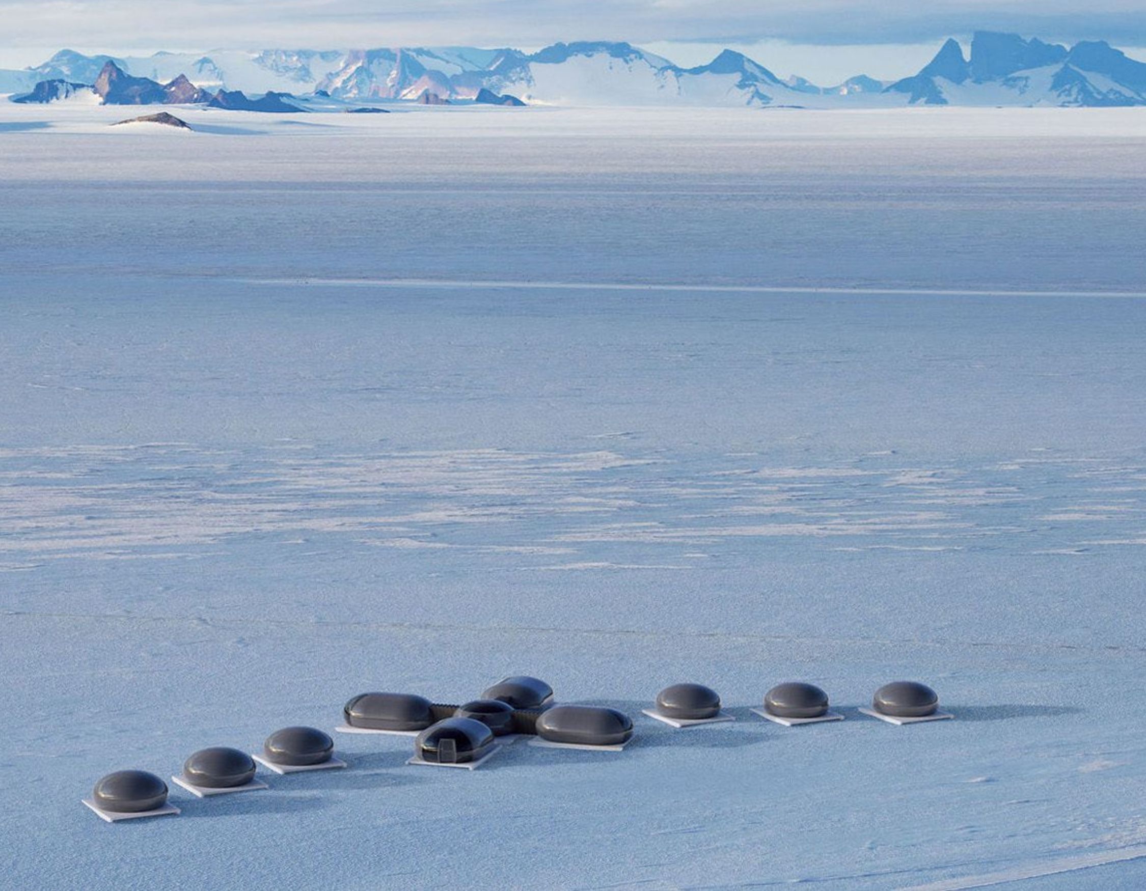 A futuristic property with multiple dome-shaped structures sits on a vast, snowy landscape, surrounded by distant mountains under a clear blue sky.