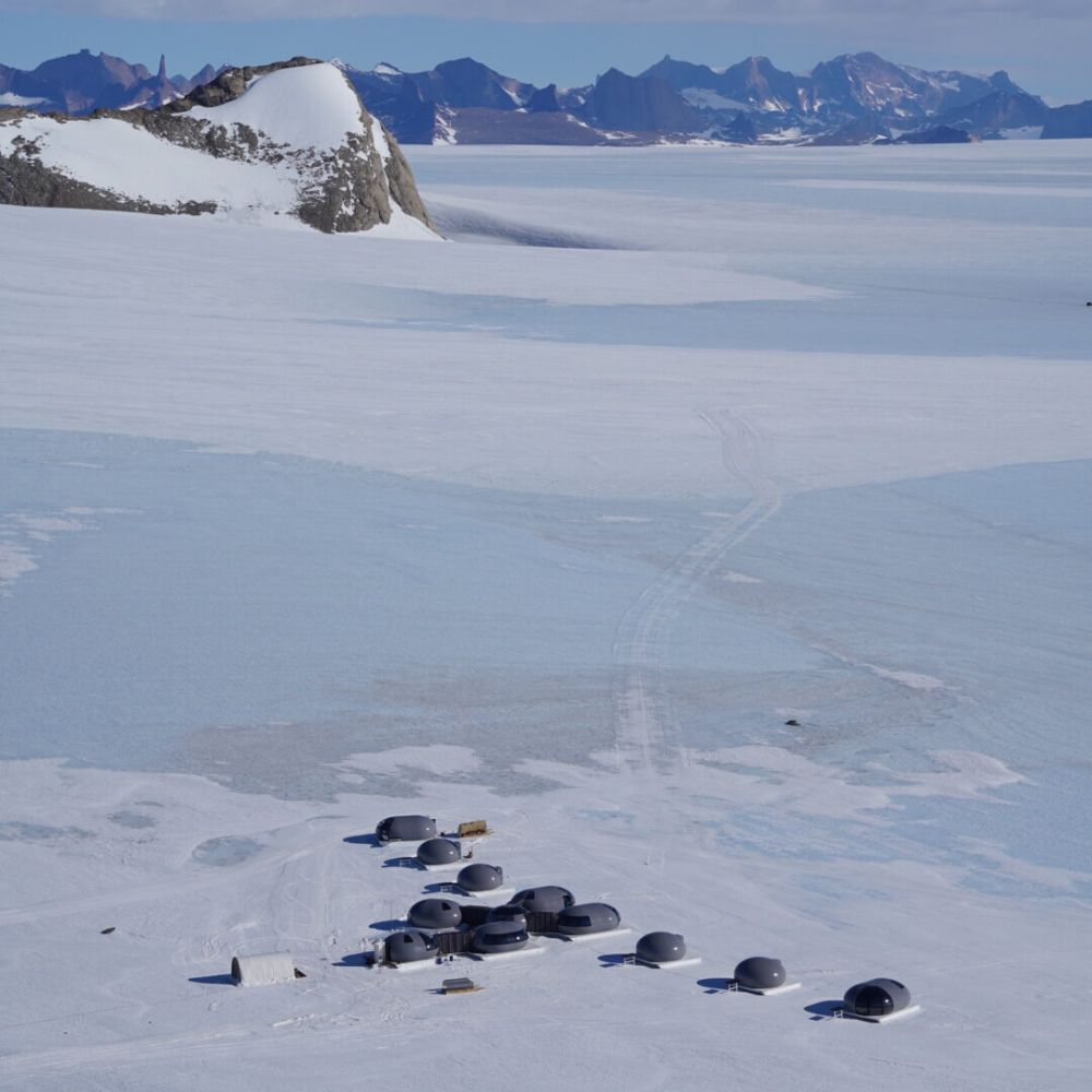 A cluster of dome-shaped structures on a vast, icy landscape, surrounded by snow and mountains in the background.