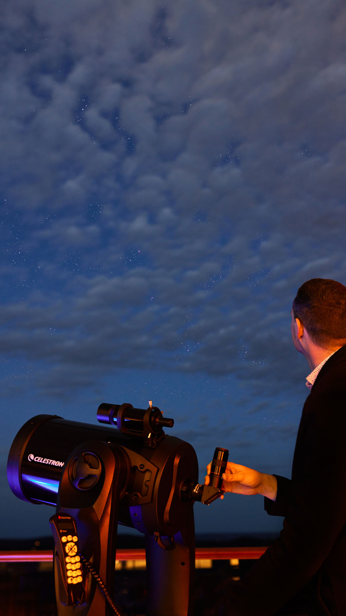 A person observes the night sky through a telescope, surrounded by clouds and stars.