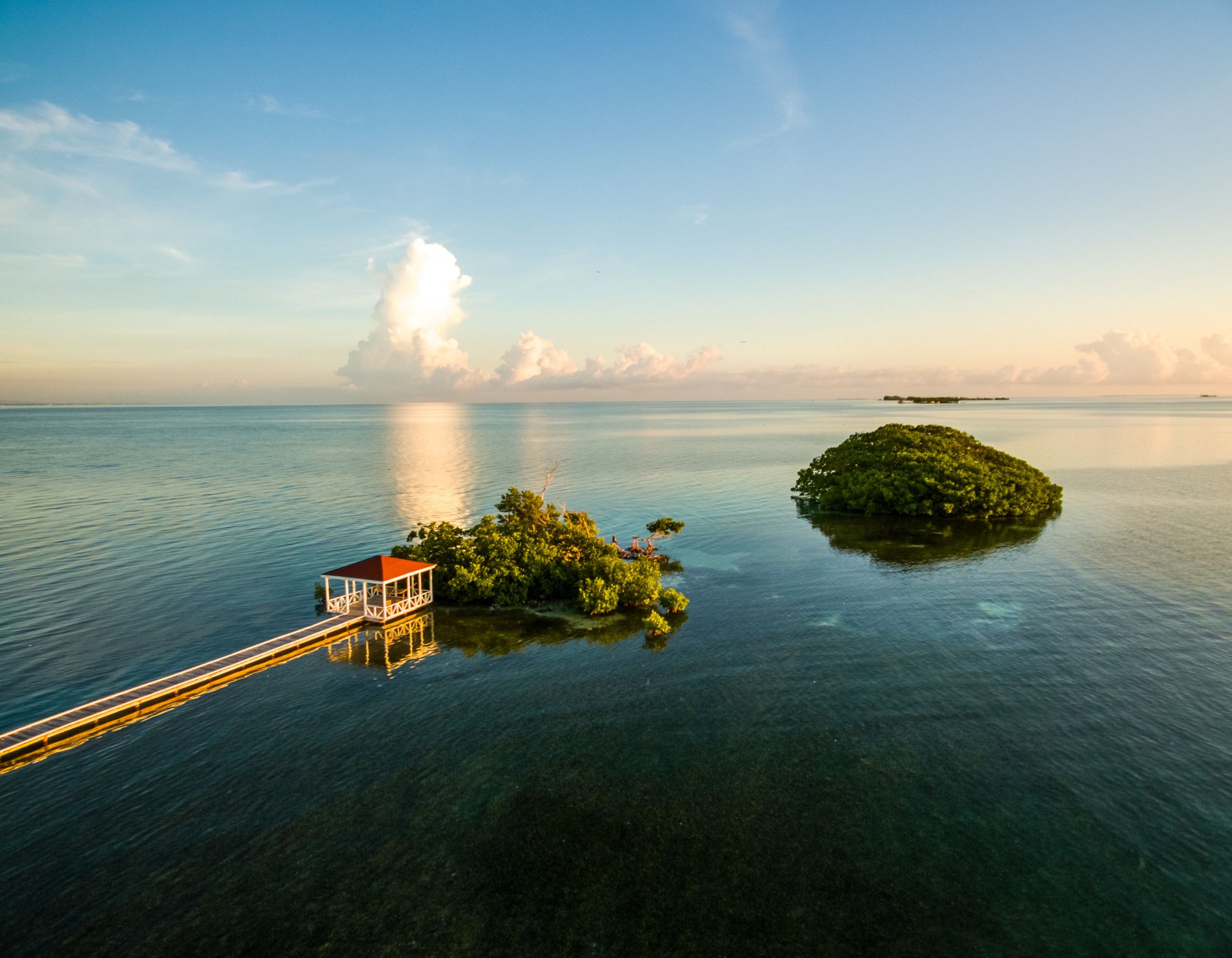 A serene ocean scene at sunset, featuring a small wooden dock leading to a lush, green island surrounded by calm waters and a colorful sky.