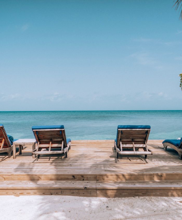Lounge chairs lined up on a wooden deck facing a calm blue ocean under a clear sky.