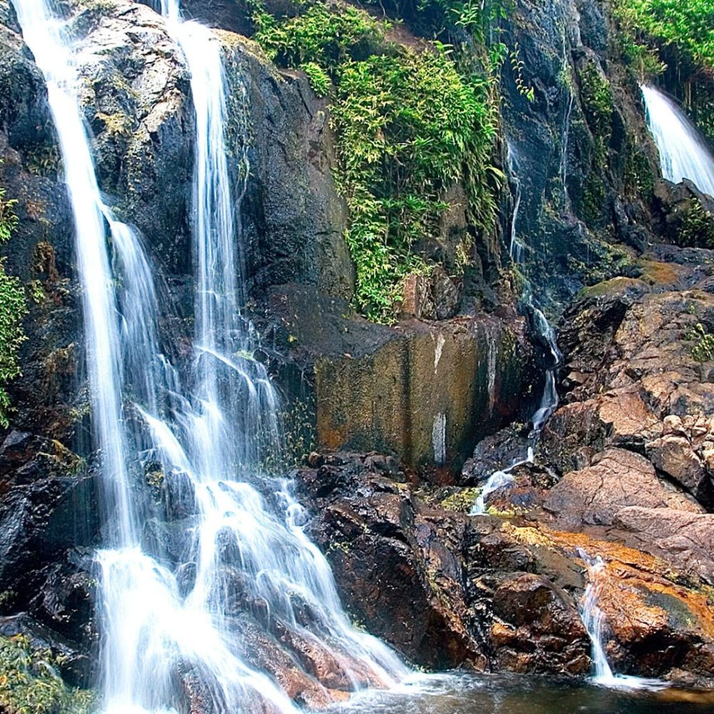 A waterfall cascading over rocky cliffs, surrounded by lush green foliage. The water flows smoothly, creating a tranquil scene.