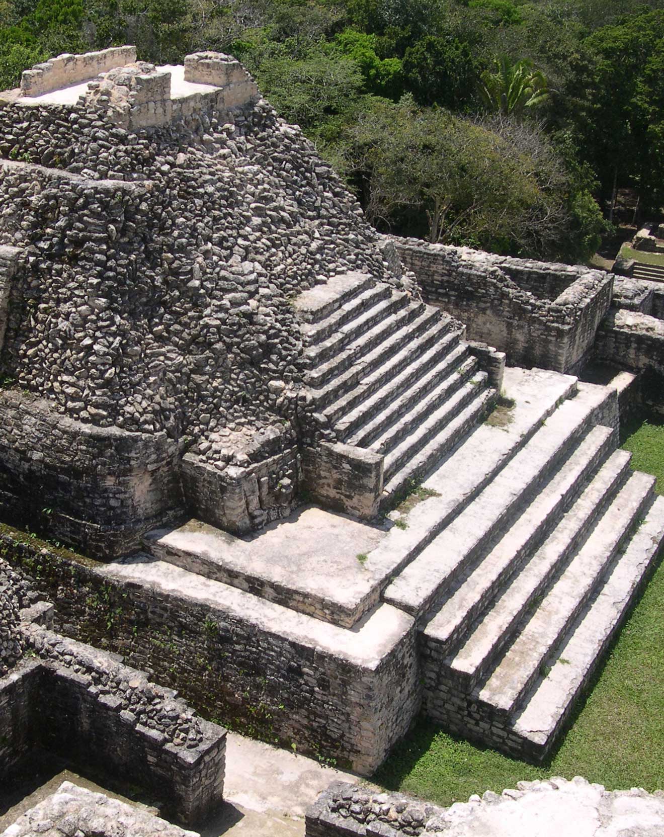 An ancient stone pyramid with stepped terraces surrounded by lush green trees.