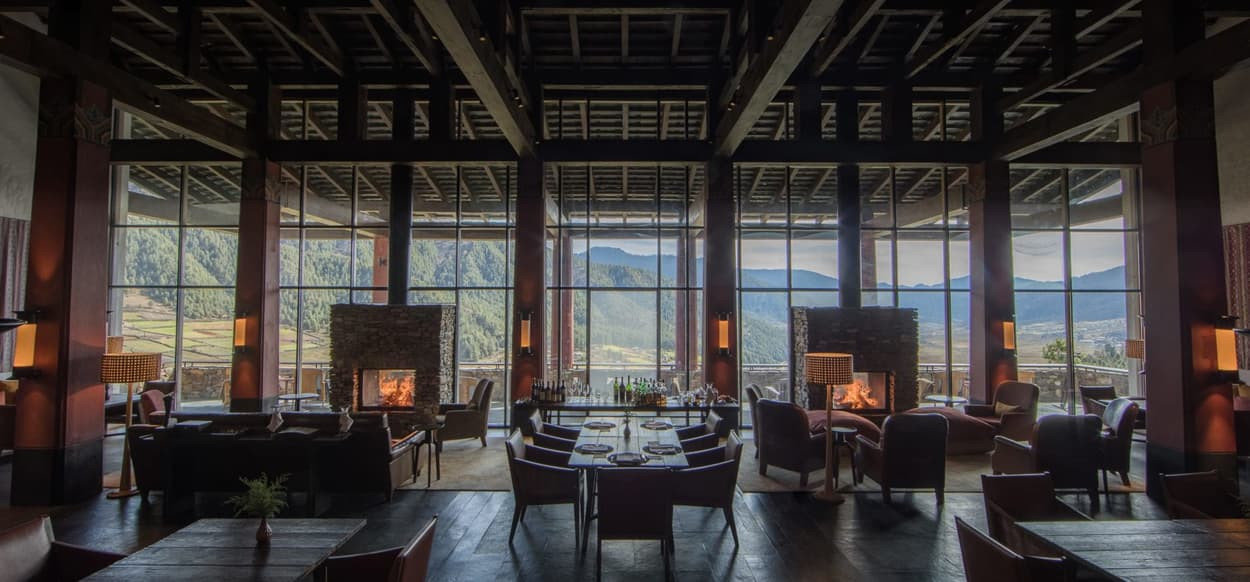 A luxurious restaurant interior featuring elegant furnishings, large windows offering stunning mountain views, and cozy fireplaces. Soft lighting and wooden accents create a warm and inviting atmosphere.