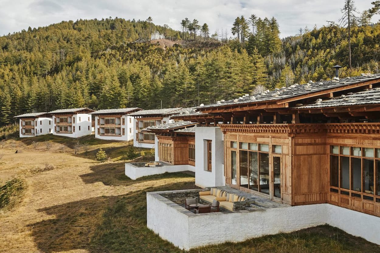 Scenic view of traditional Bhutanese-style lodges nestled on a hillside amidst lush greenery and distant mountains.