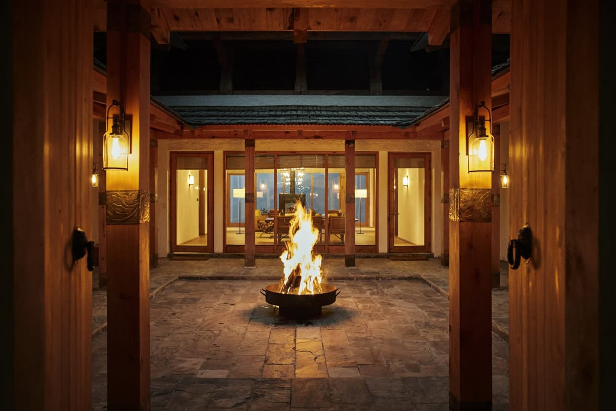 A cozy interior courtyard featuring a central fire pit surrounded by warm wooden furnishings and lanterns, creating a welcoming atmosphere in the evening.