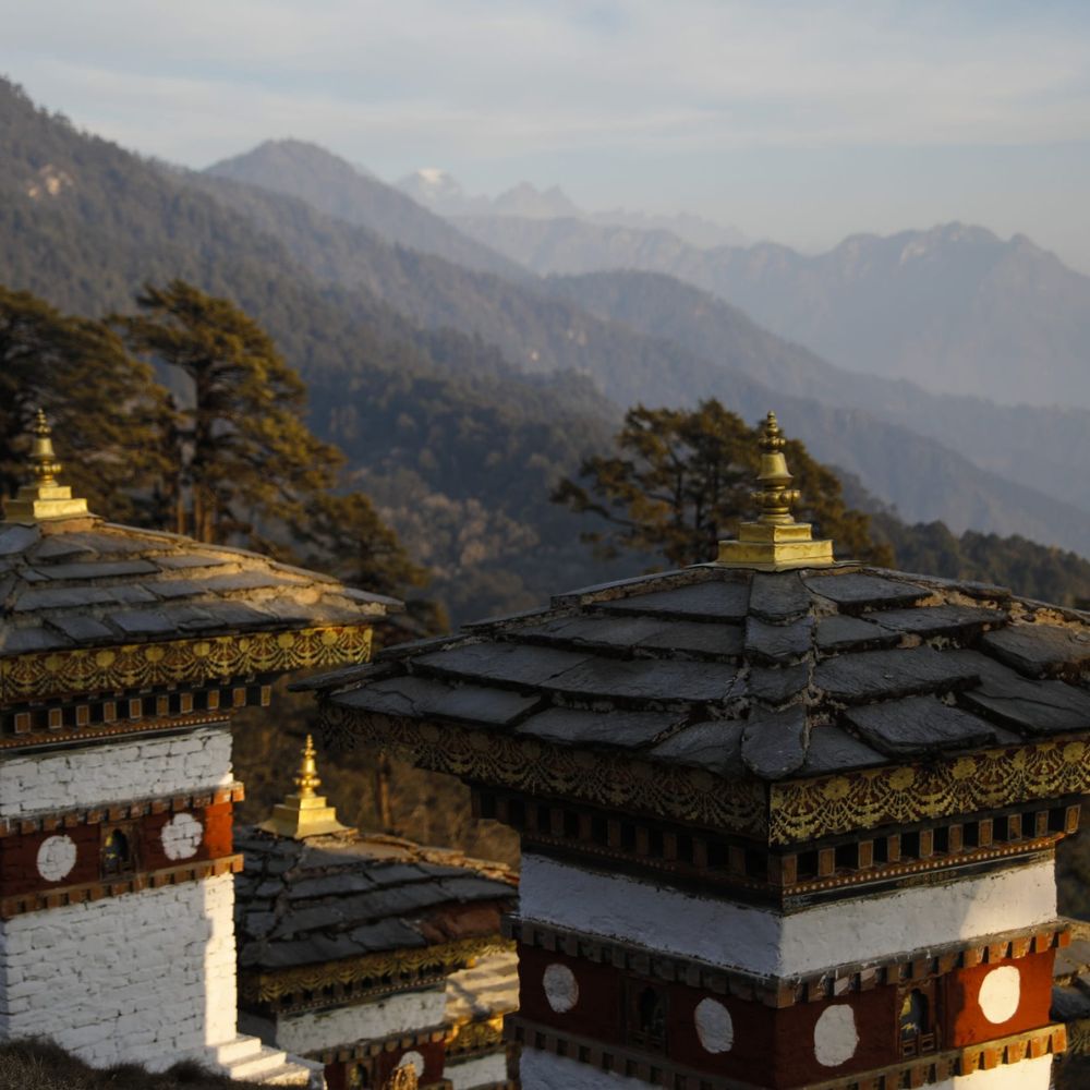 Stupas with ornate rooftops in the foreground, set against a backdrop of majestic mountains and a clear sky.