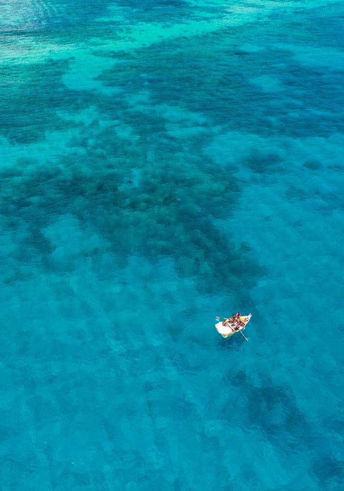 A small boat with people is floating on vibrant turquoise waters, revealing patterns of the ocean floor beneath.
