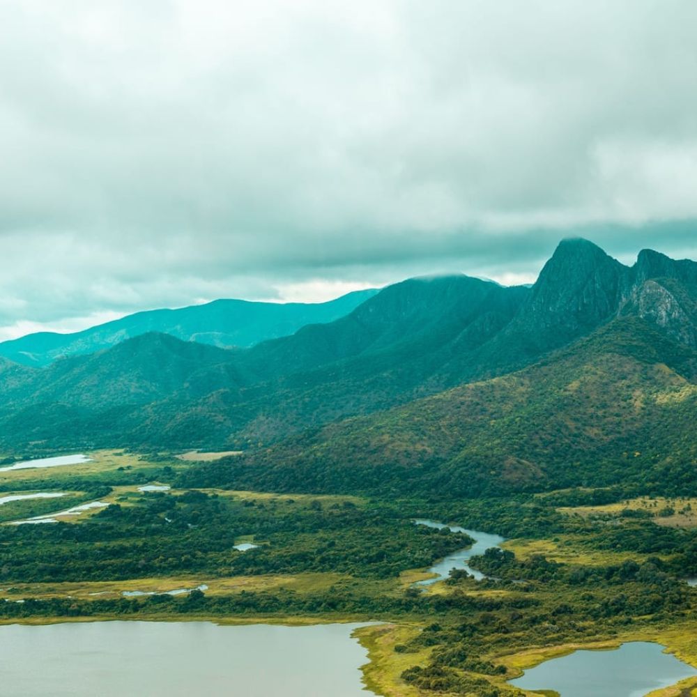 Lush green mountains rise in the background, surrounded by winding rivers and expansive wetlands under a cloudy sky.