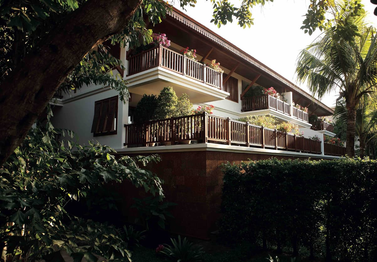 A multi-level villa surrounded by lush green foliage and tropical plants. Balconies adorned with colorful flowers create a vibrant and inviting atmosphere.