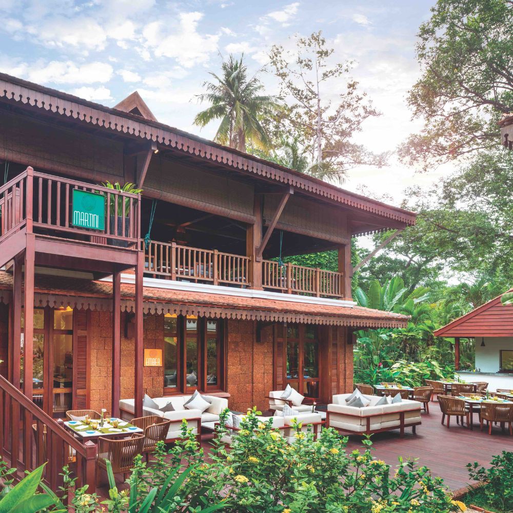 A beautifully designed wooden tropical villa surrounded by lush greenery. The two-story structure features a spacious deck with comfortable seating, showcasing a harmonious blend of nature and architecture.