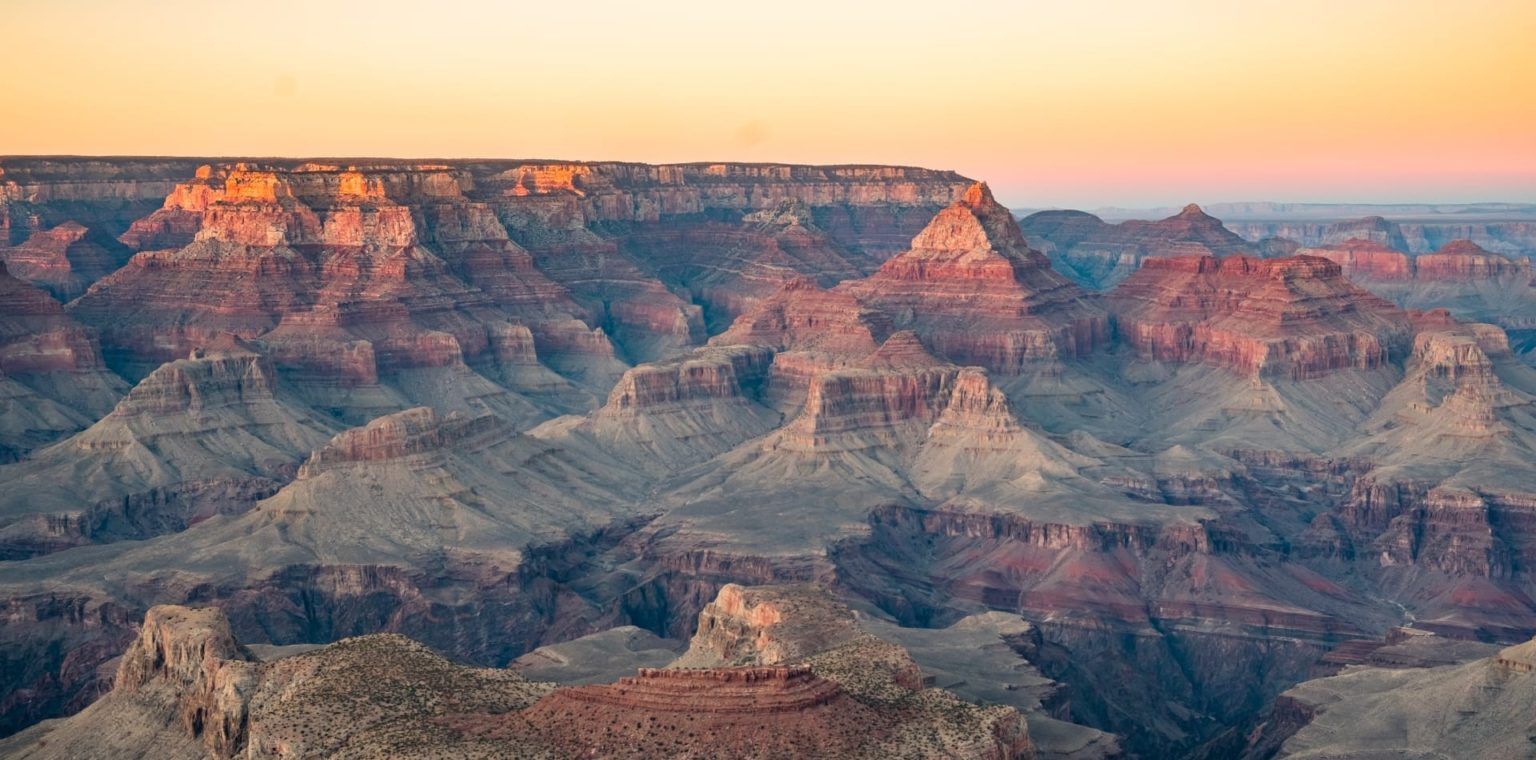 Panoramic view of the Grand Canyon showing layered rock formations under a soft sunset sky.