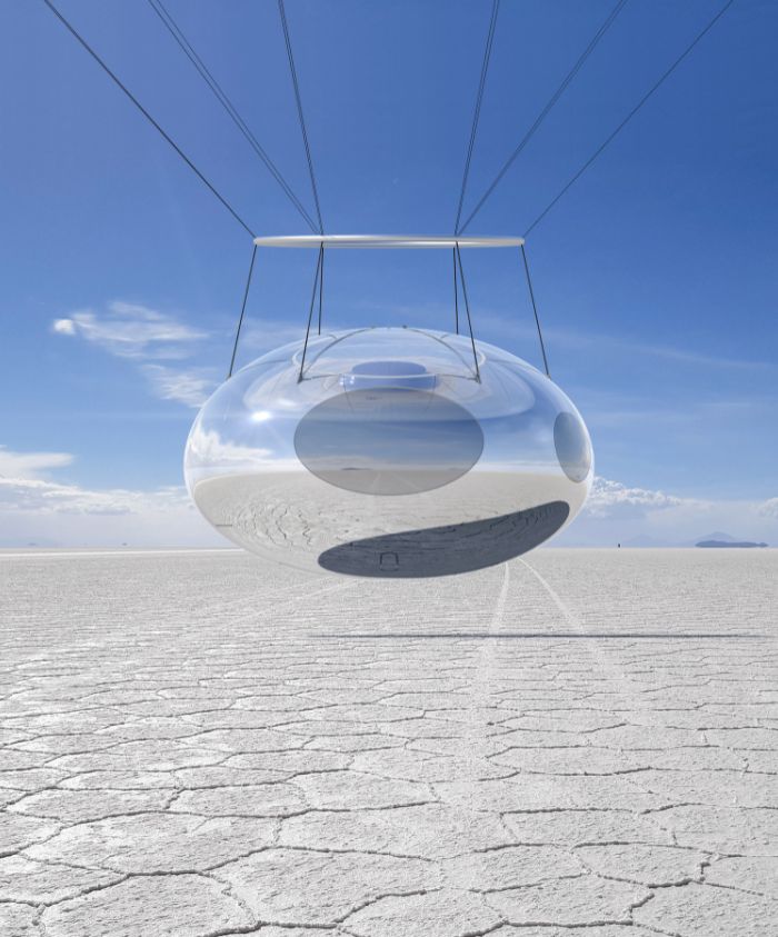 A futuristic, oval-shaped pod suspended by cables above a vast, cracked salt flat. The pod has a reflective surface, contrasting with the clear blue sky.